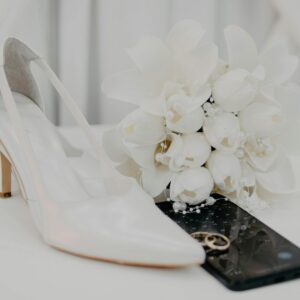 Elegant display of white bridal shoes, bouquet, and rings symbolizing a wedding celebration.
